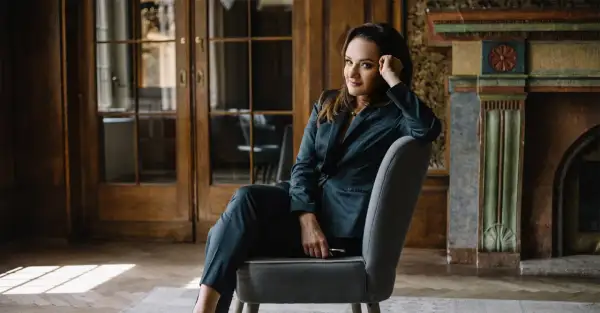 Kobieta w garniturze siedzi na krześle w eleganckim wnętrzu.